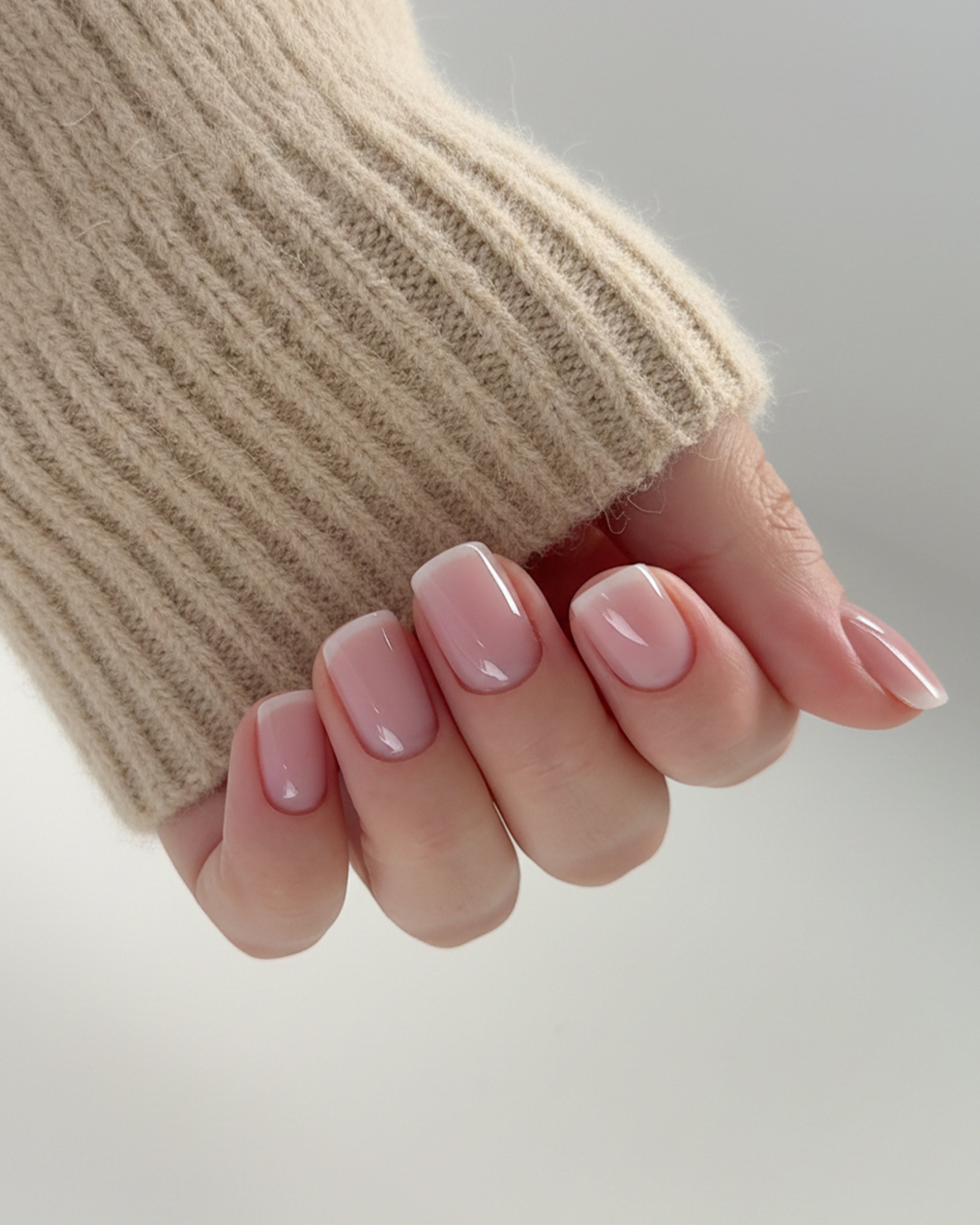 Close-up of a hand with pink nail polish wearing a beige knit sleeve on a light background